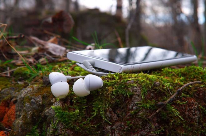 white earphones with smartphone on moss-covered stone, shallow depth of field