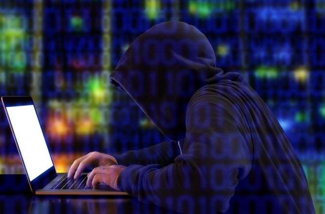 Hacker in a green hoody sitting in front of a notebook with colored server background and binary streams cybersecurity concept