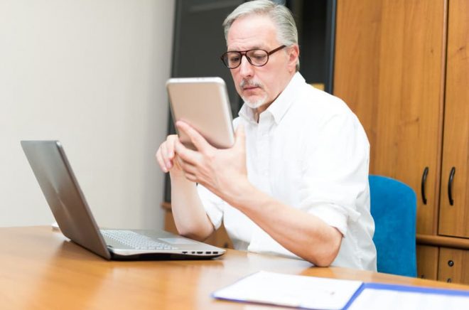 Man using a tablet and a laptop in his office