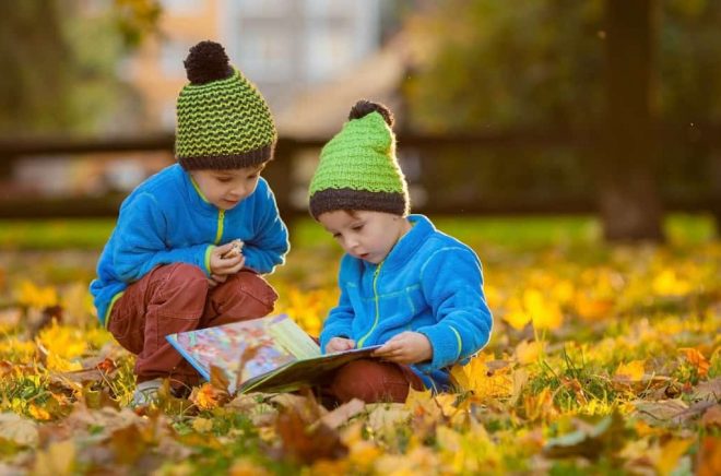 Two boys, reading a book on a lawn in the afternoon, eating snacks, autumn sunset time