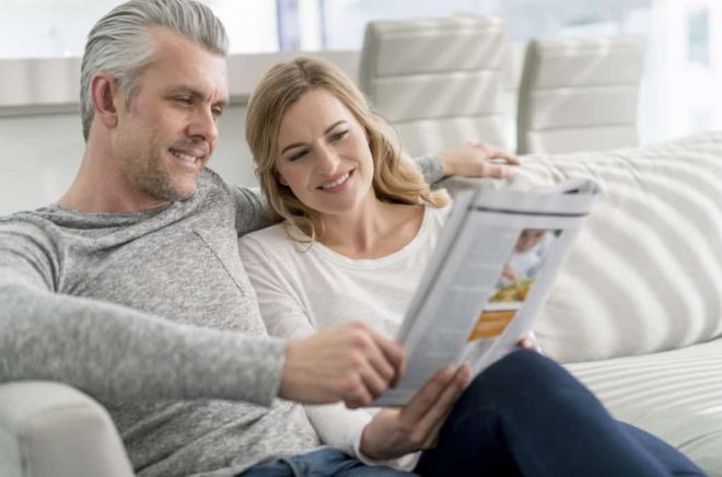 Happy loving couple at home reading a magazine and sitting on the sofa relaxing