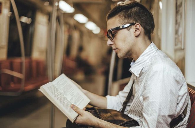 Young man is reading a book on the underground. Candid shot.