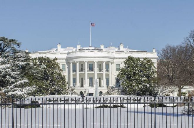 White House and grounds are covered with snow beneath a bright blue sky.