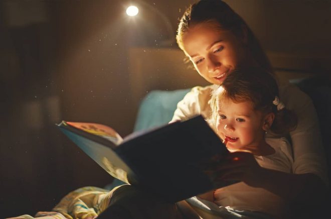 mother and child girl reading a book in bed