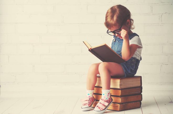 happy child little girl with glasses reading a books