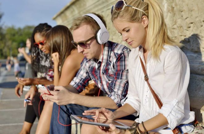 Young beautiful friends together outdoors, listening music, using tablet PC and smartphone.